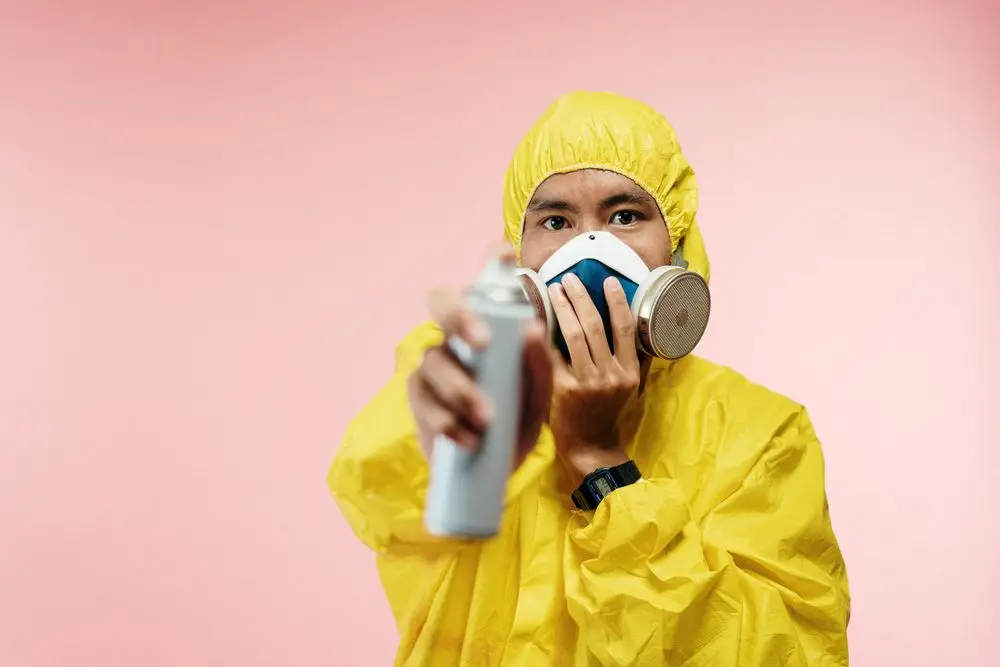 A technician in a yellow suit and respirator with a spray can.