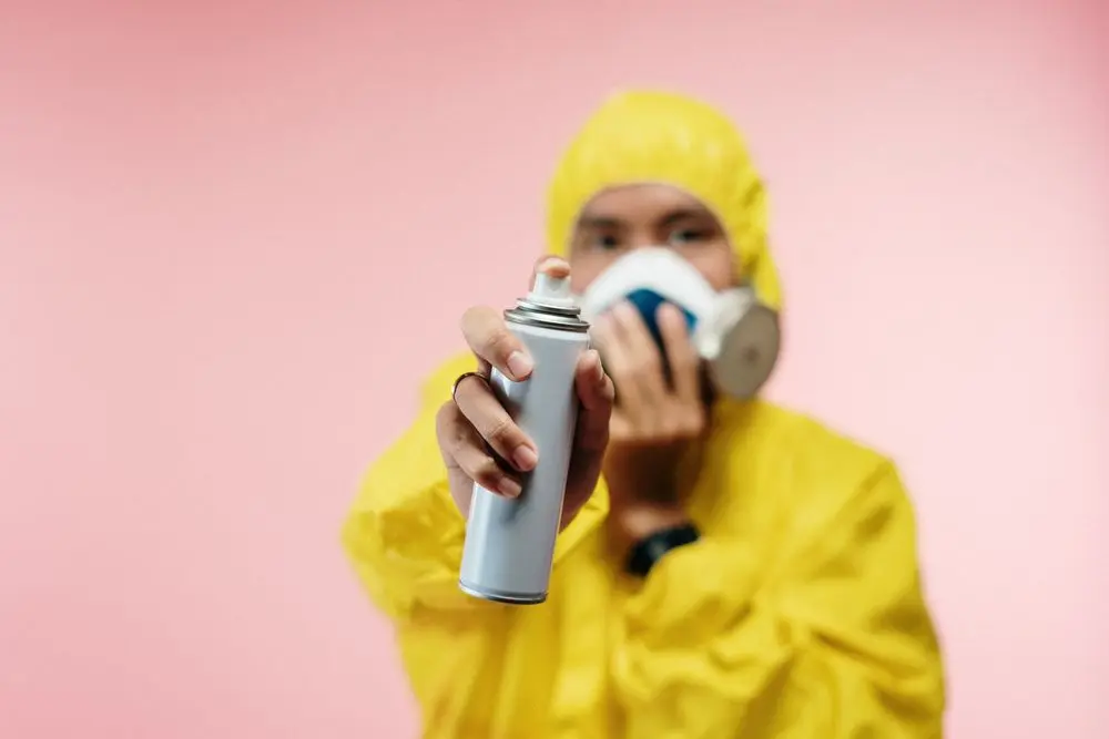 A technician in a yellow suit and respirator spraying.